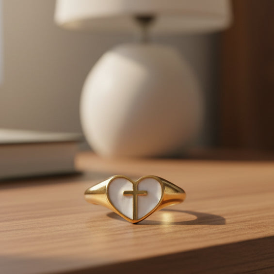 Gold ring with a heart-shaped design and cross symbol on a marble surface