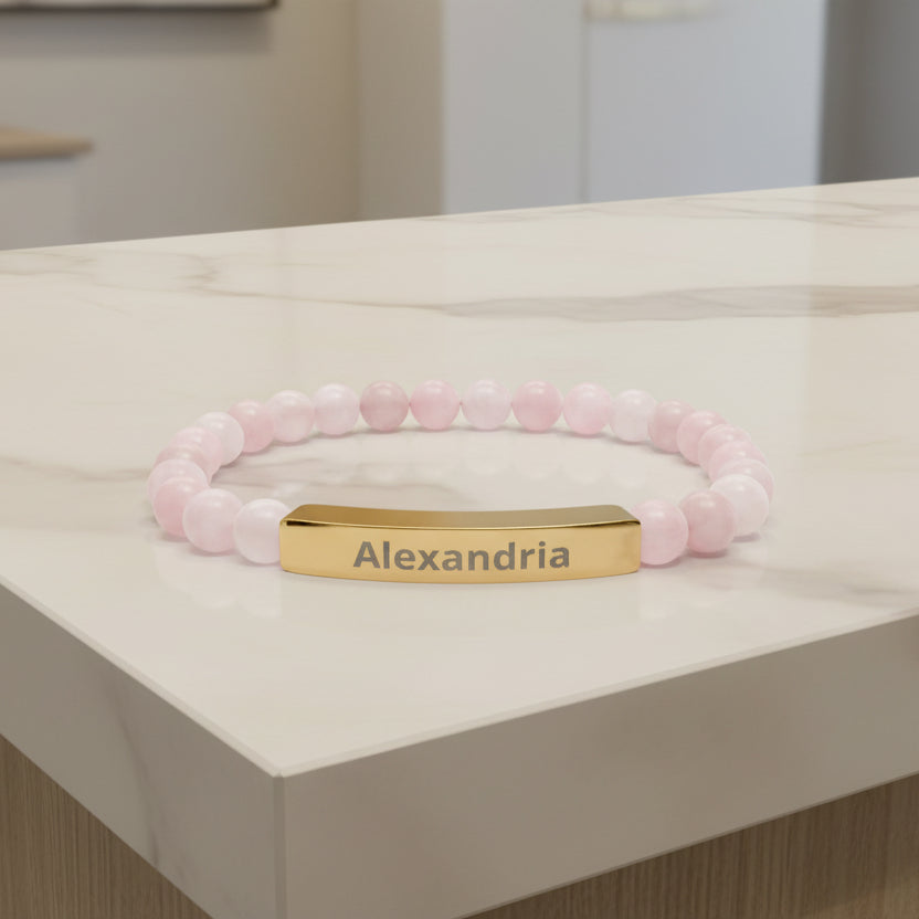 Pink beaded bracelet with a gold tag displaying 'Alexandria' on a white background