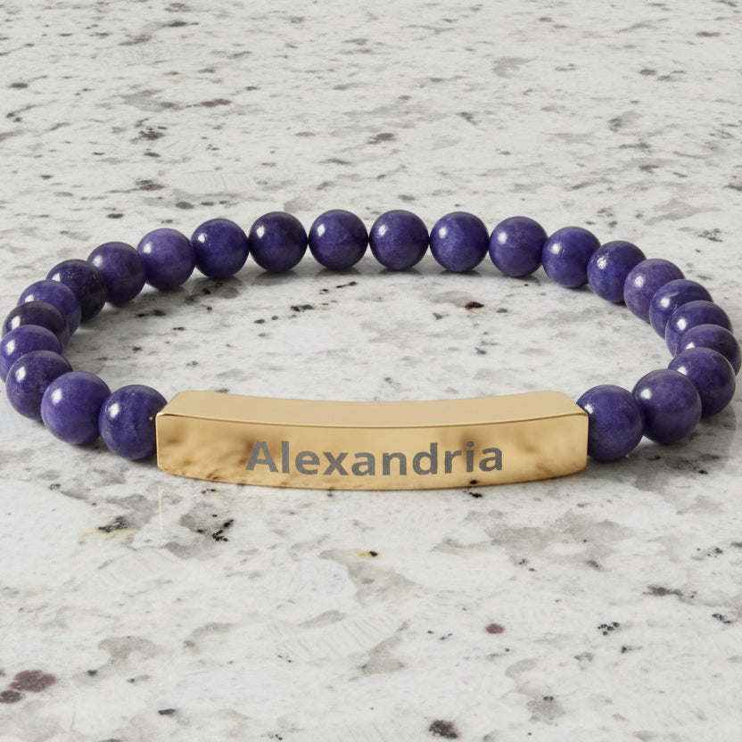 Bracelet with purple beads and gold tag displaying 'Alexandria' on a white background