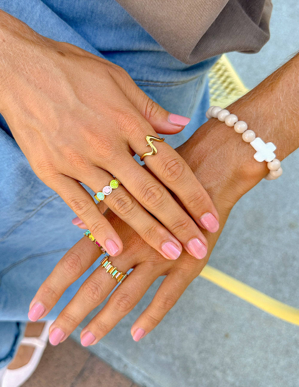 Close-up of two hands with colorful rings and pink nail polish, wearing a beaded bracelet.