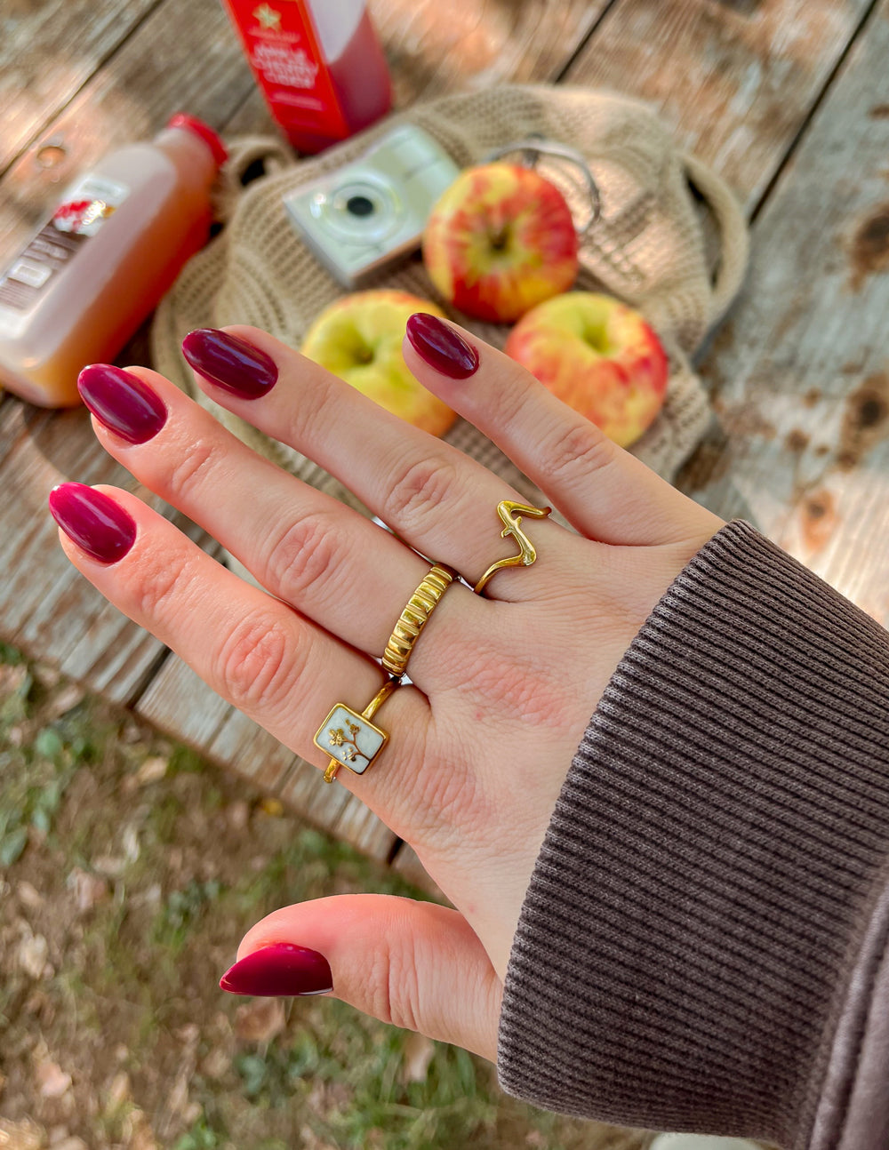 Hand with gold rings and red nail polish holding a woven basket with apples and juice bottles.