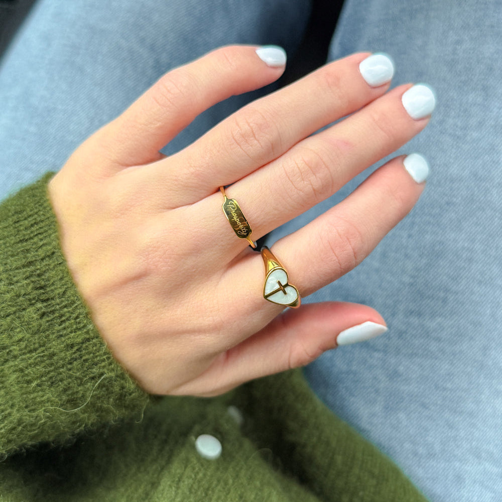 Hand wearing a ring with a green gemstone, against a blurred background