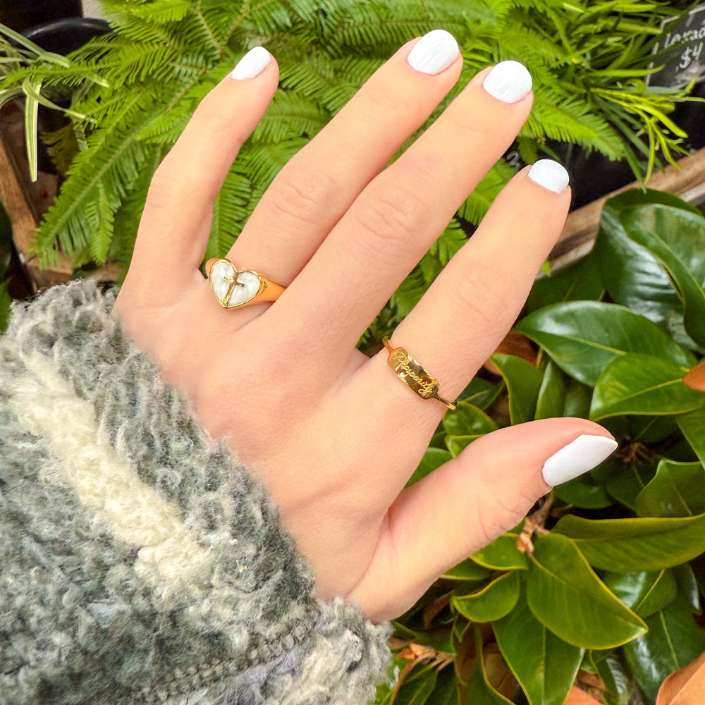 Hand with two rings against a green leafy background