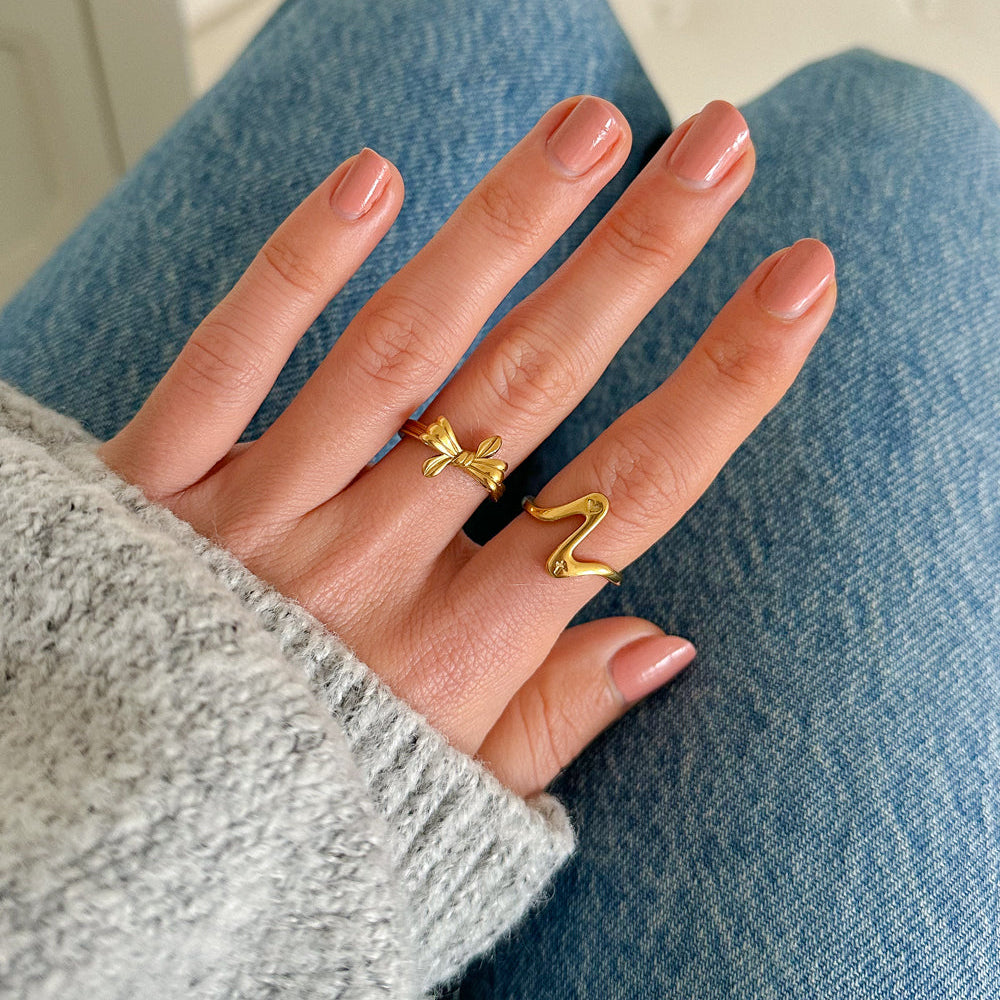 Hand wearing a gold ring with a bow design on a light blue fabric background