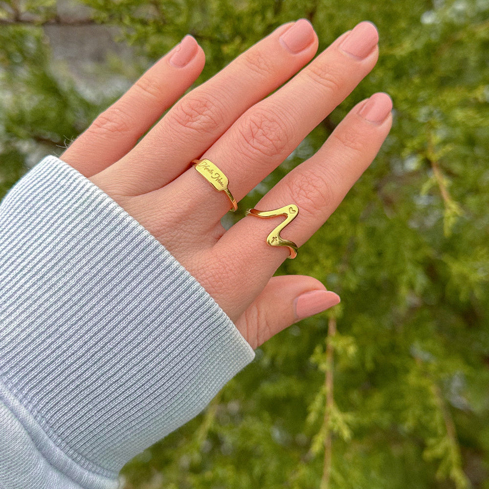 Hand wearing a gold ring with a blurred green background