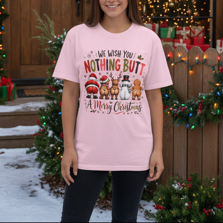 A light pink short-sleeve crewneck t-shirt featuring a Christmas-themed graphic with the text 'WE WISH YOU NOTHING BUT A Merry Christmas' and illustrations of Santa, a reindeer, a snowman, and a gingerbread man.
