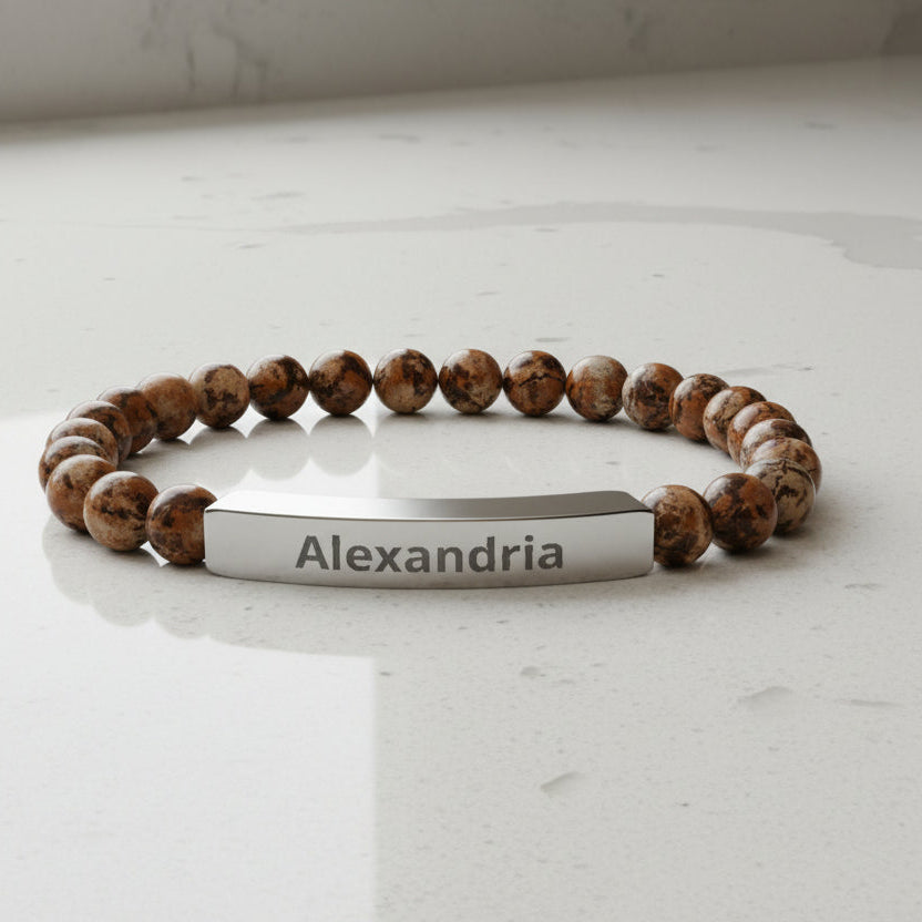 Bracelet with brown beads and a silver tag displaying 'Alexandria' on a white background