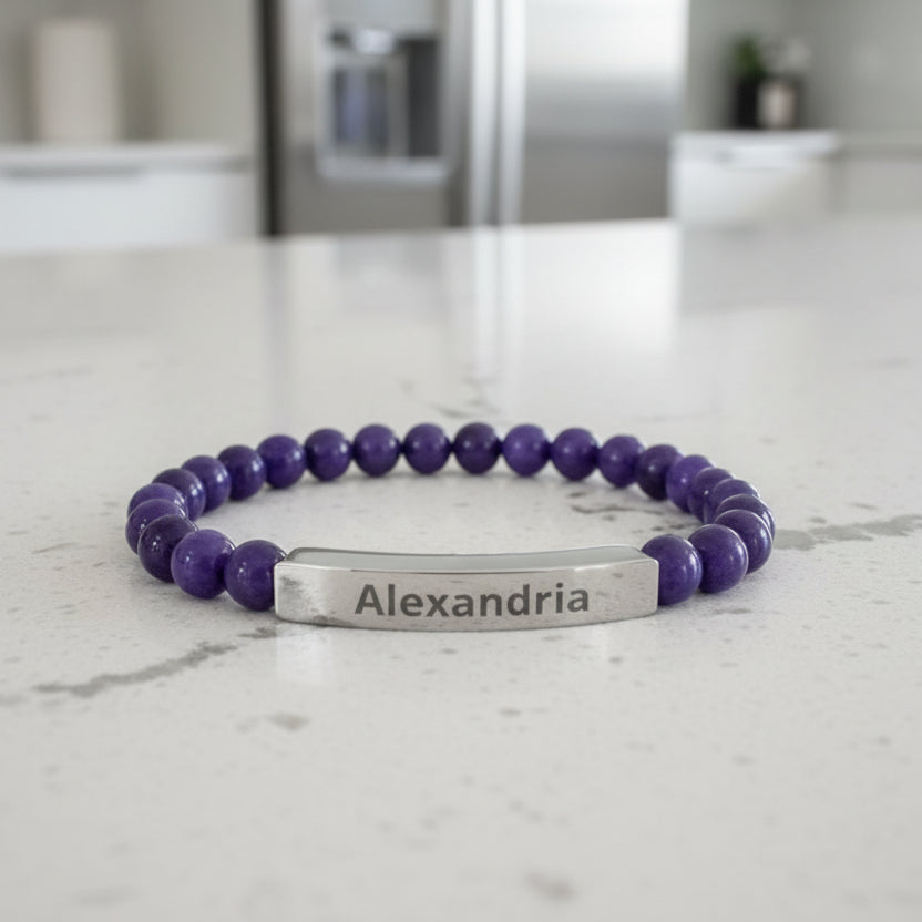 Purple beaded bracelet with a silver tag on a light gray background