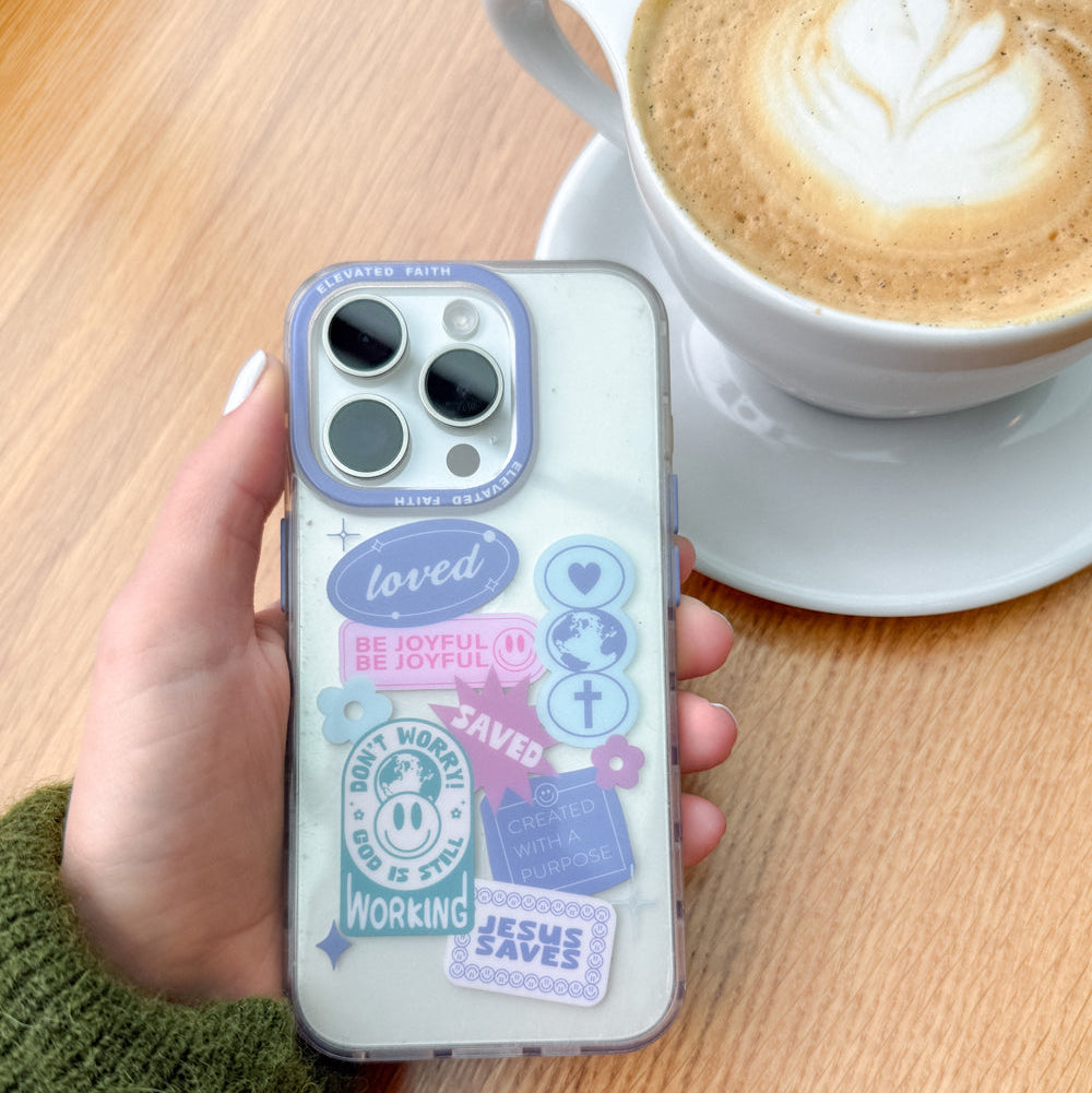 Phone case with motivational phrases held by a hand next to a cup of coffee on a wooden table.