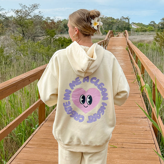 Person wearing a cream-colored hoodie with a heart graphic and text on a wooden boardwalk.