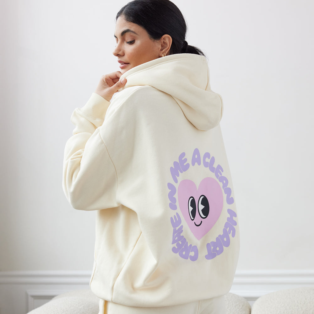 Person wearing a cream-colored hoodie with a heart design and text on the back, sitting on a couch.