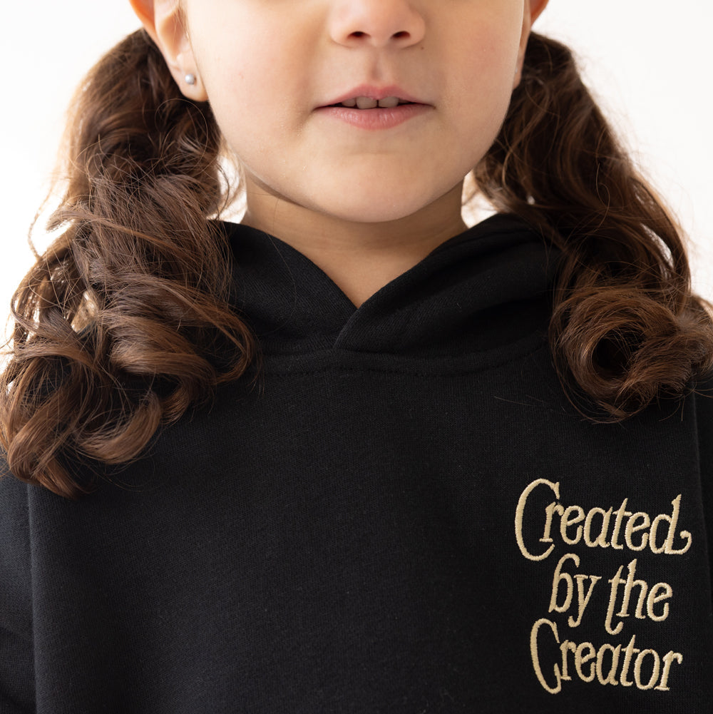 Black hoodie with 'Created by the Creator' text worn by a child, on a white background