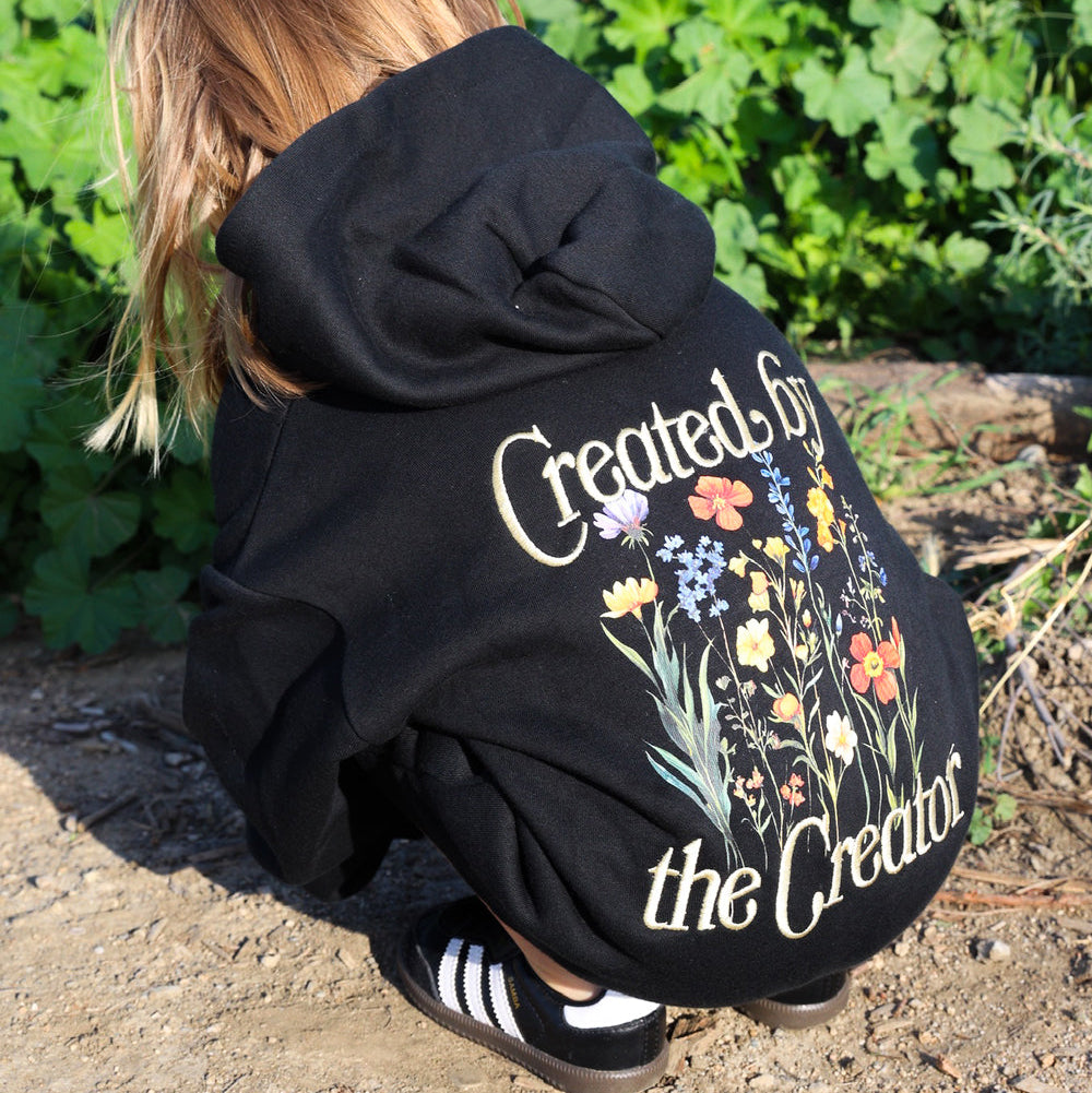 Person wearing a black hoodie with floral design and text in an outdoor setting
