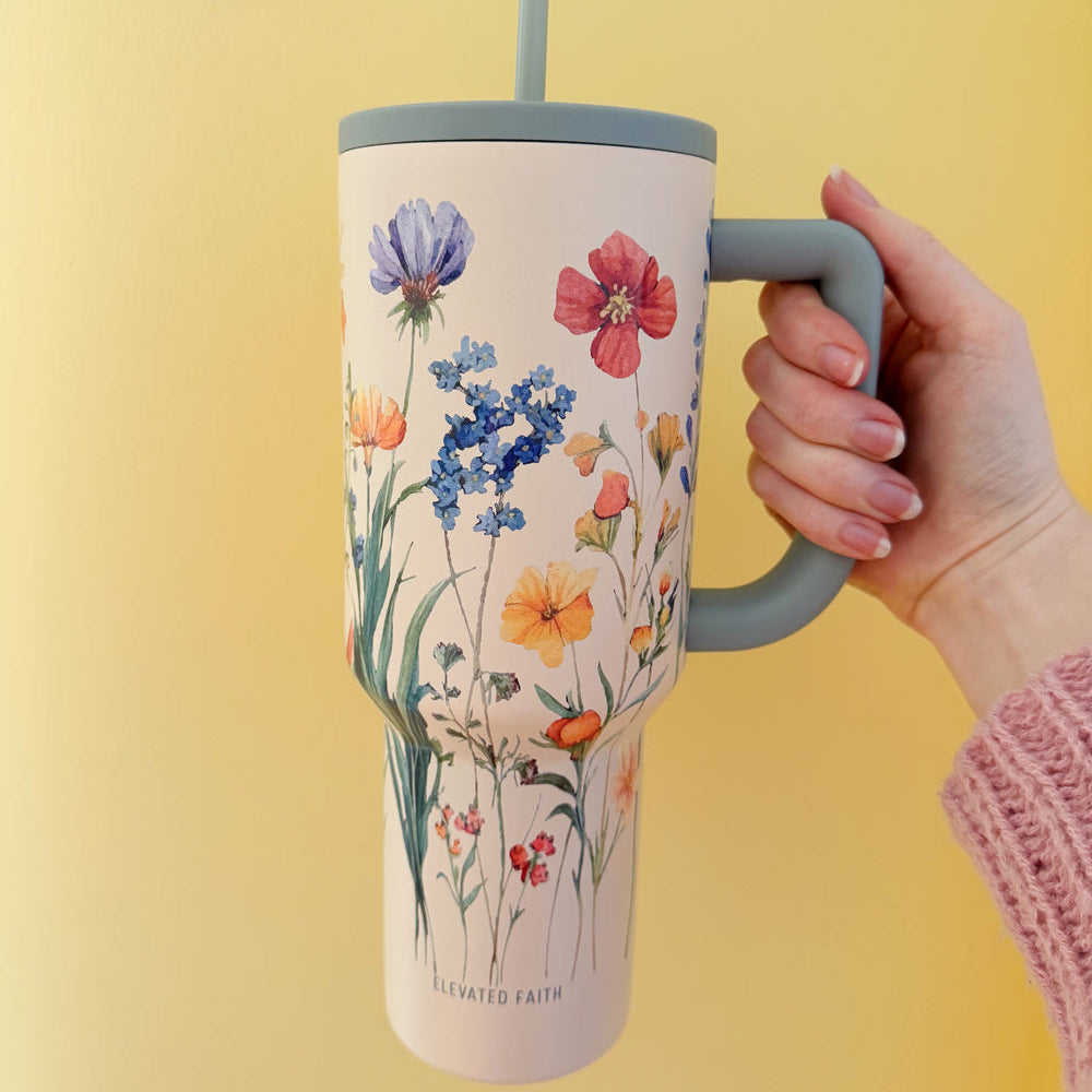 Tumbler with floral design held by a hand against a yellow background