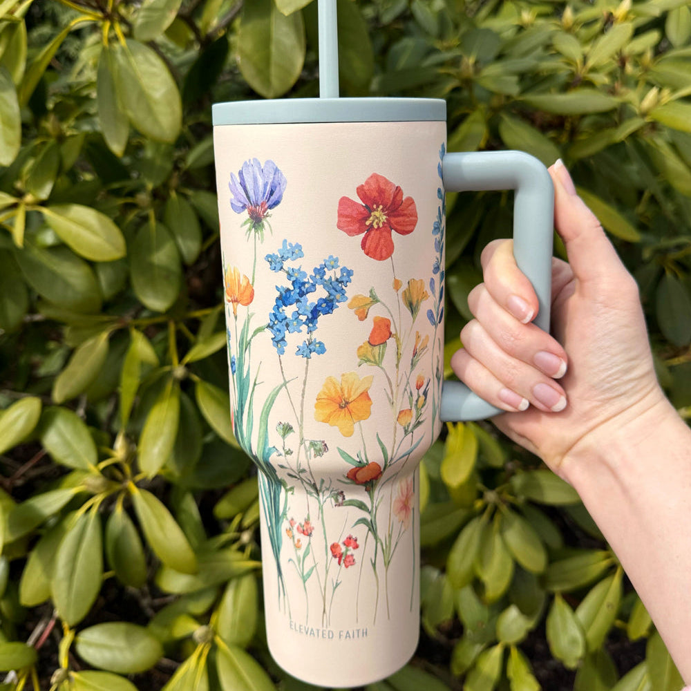 Hand holding a floral-patterned tumbler with a straw against a green leafy background