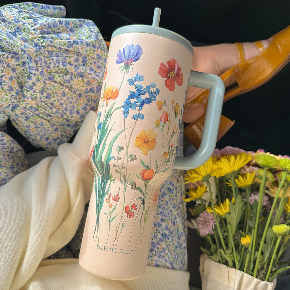 Person holding a tumbler with floral design and flowers in the background