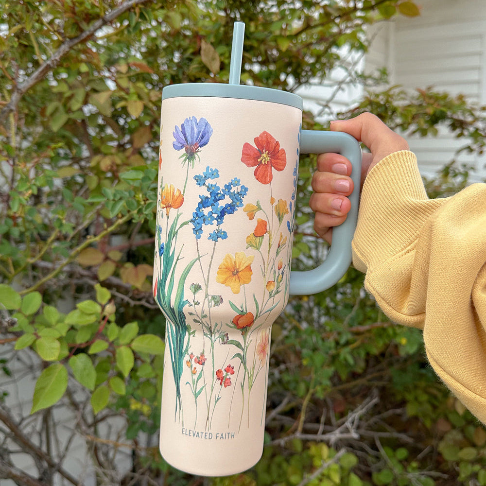 Person holding a floral-patterned tumbler with a straw, outdoors.