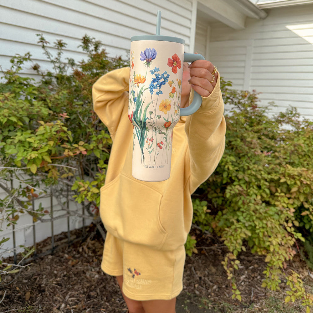 Person holding a floral mug outdoors with a house and garden in the background