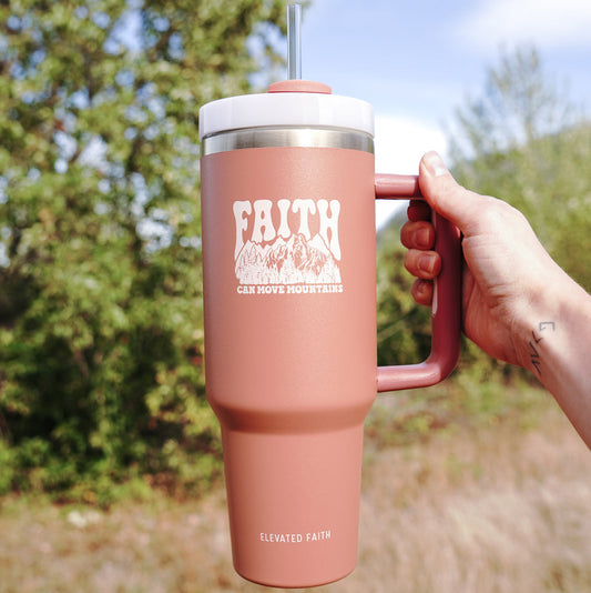 Pink travel mug with 'FAITH' text held outdoors
