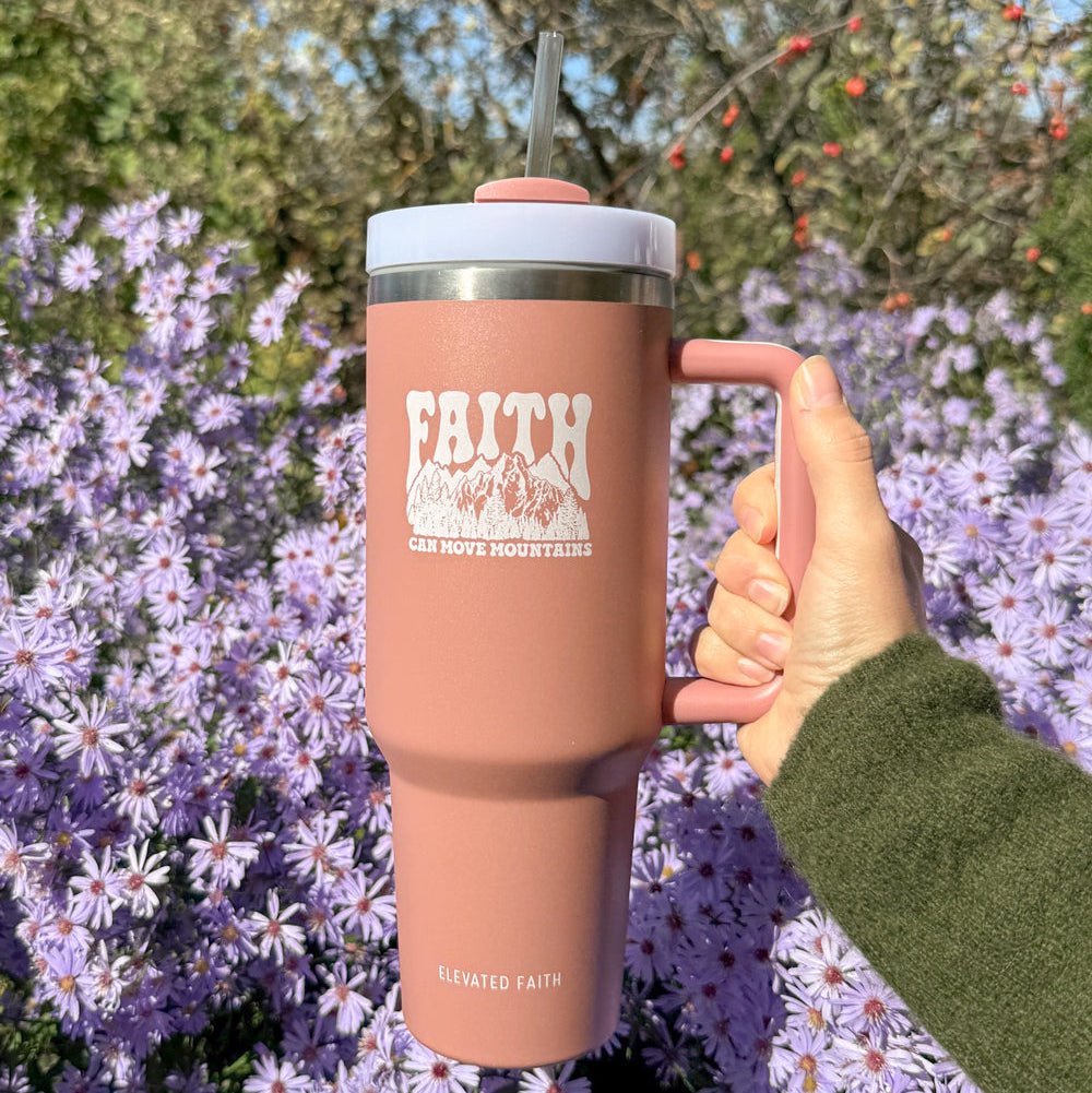 Person holding a pink tumbler with 'Faith' text against a floral background