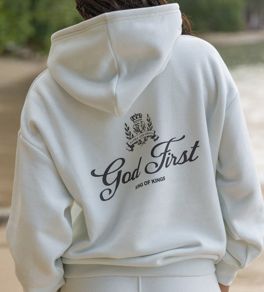 Person wearing a white hoodie with 'God First King of Kings' text on the back, outdoors.