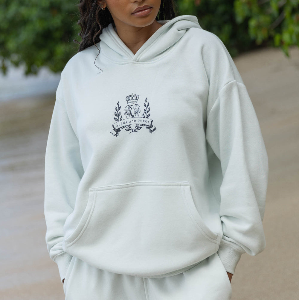 Person wearing a light gray hoodie with a logo, standing outdoors.