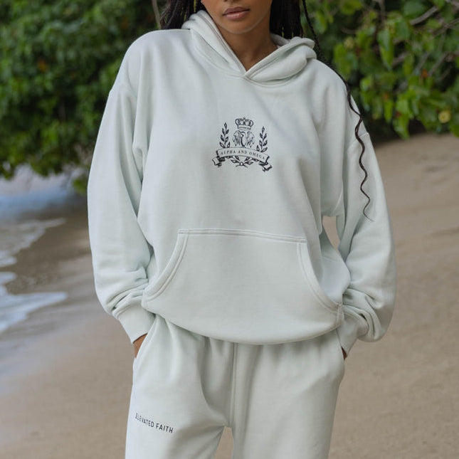 Person wearing a light gray hoodie and pants with a logo on a beach