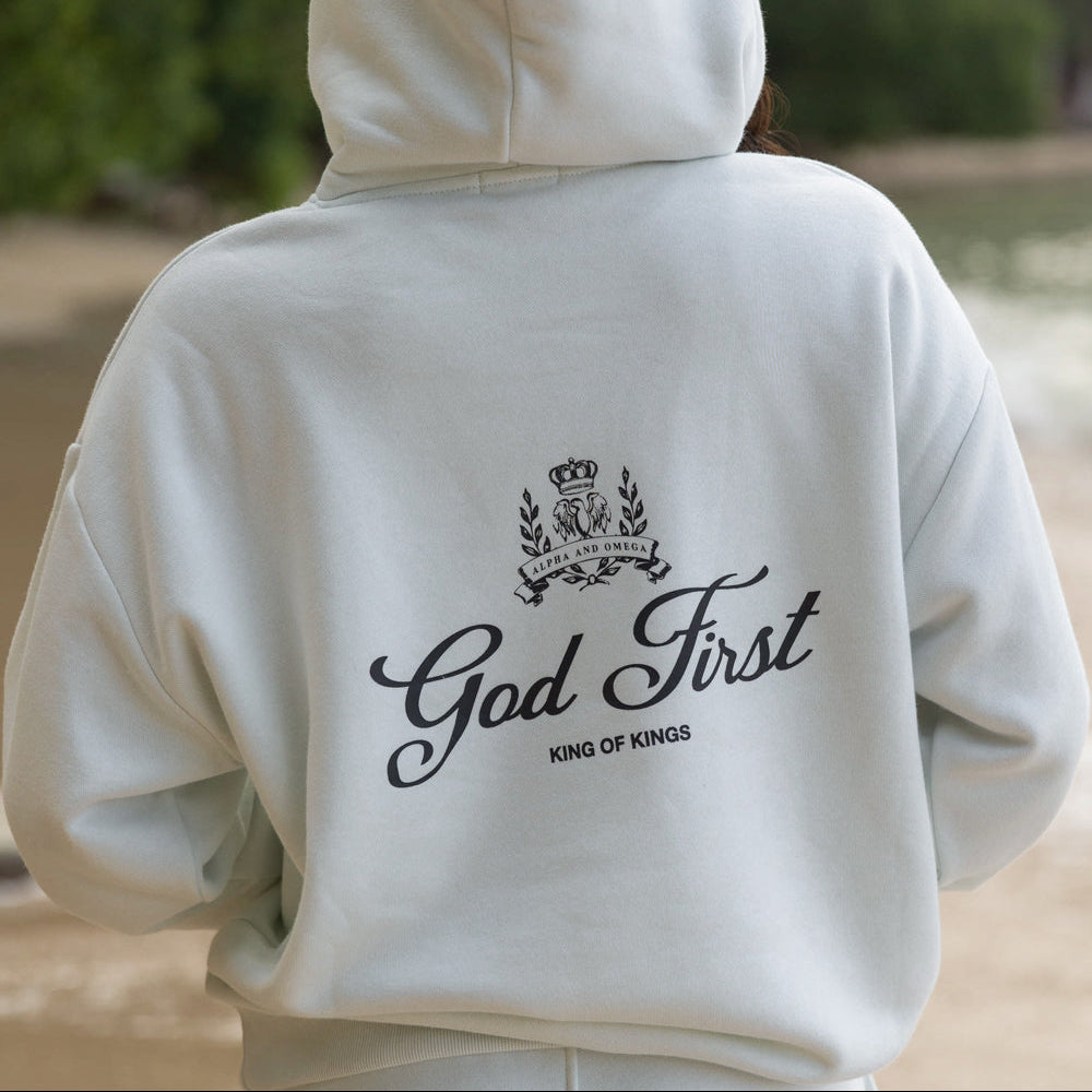 Person wearing a white hoodie with 'God First' text on the back outdoors.