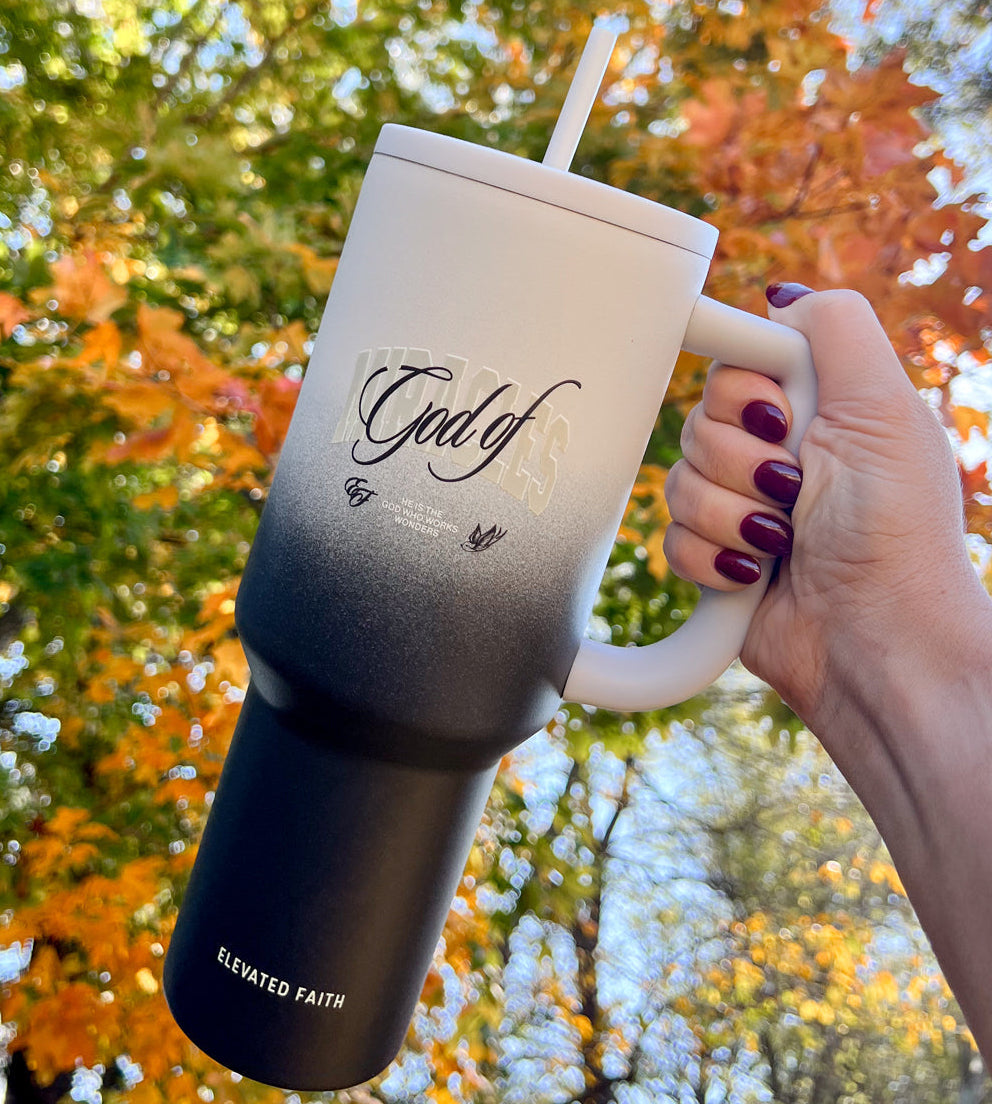 Person holding a mug with 'God of' text against an autumn tree background