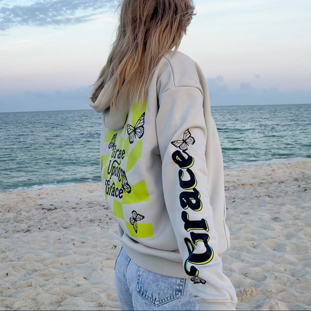 Person wearing a hoodie with text and butterfly designs on a beach