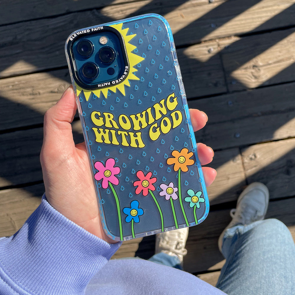 Phone case with 'Growing with God' text and floral designs held by a person on a wooden surface.