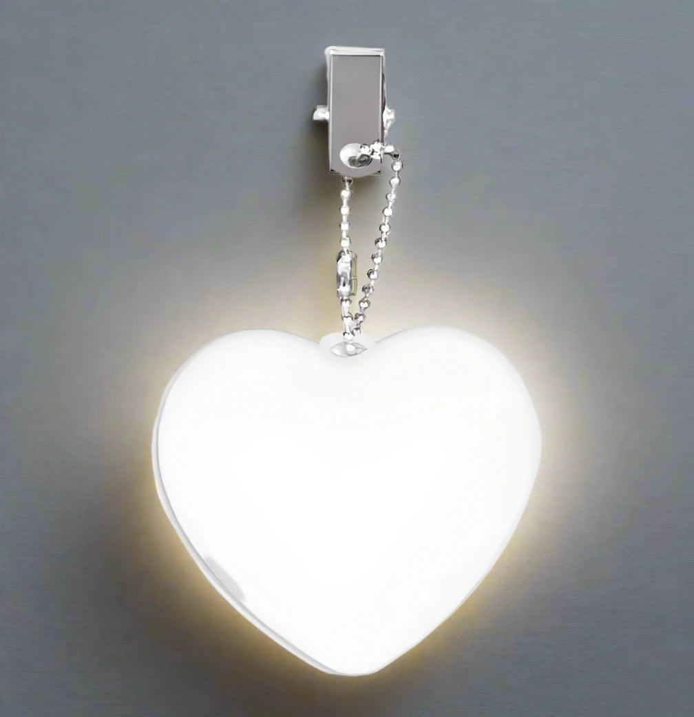 A heart-shaped white night light with a silver clip and ball chain, shown glowing against a dark gray background.