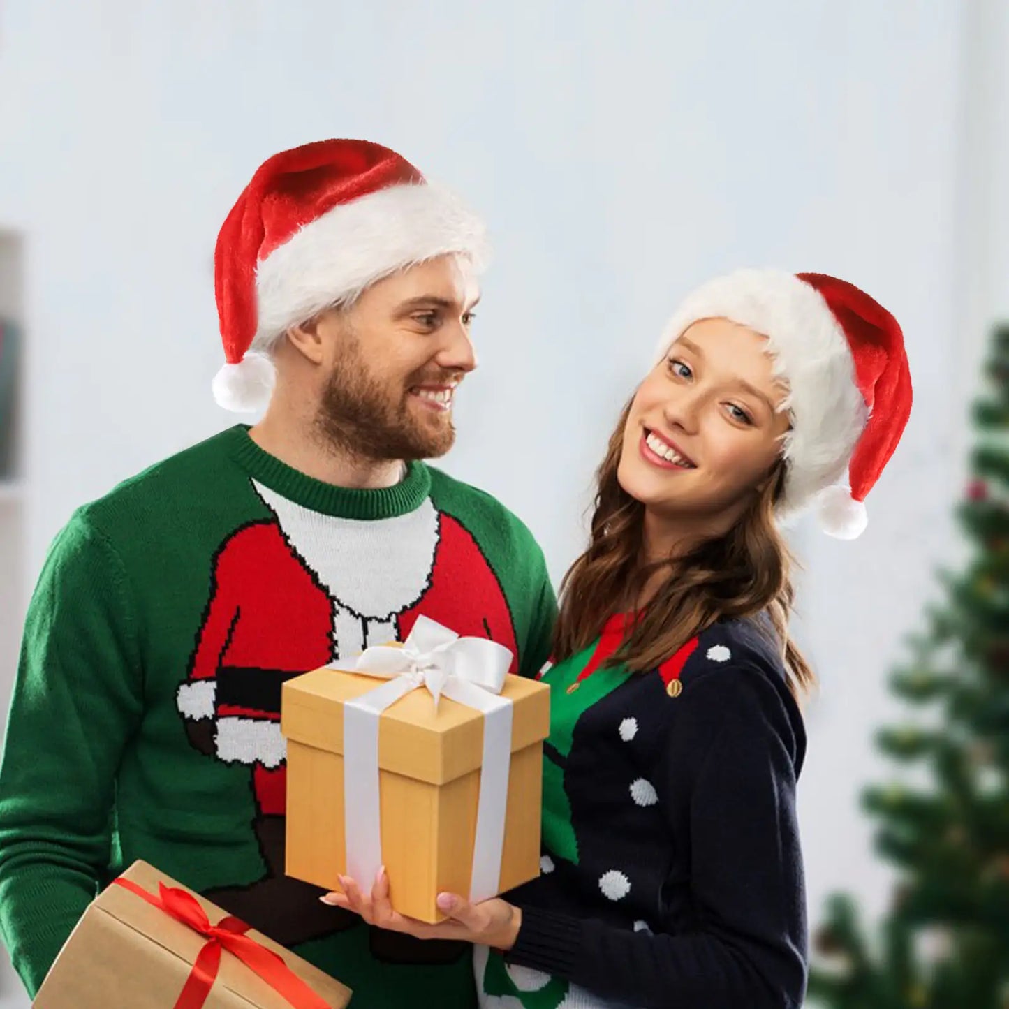 Two people wearing Santa hats holding Christmas presents with a blurred Christmas tree in the background.