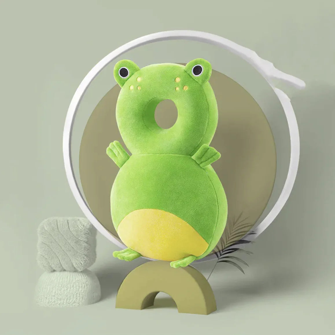 Green plush toy with a yellow belly on a stand against a light gray background
