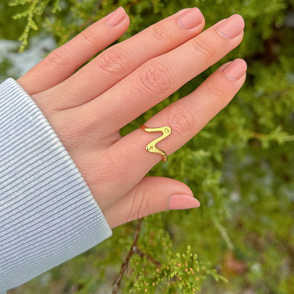 Hand wearing a gold ring with a green leafy background