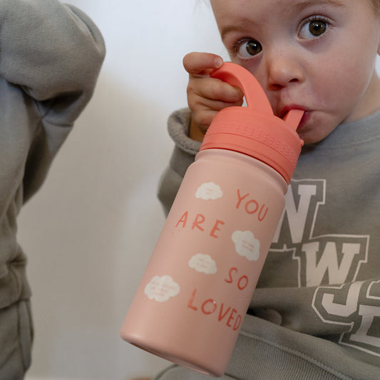 Child holding a pink sippy cup with 'You are so loved' text, wearing a gray hoodie.