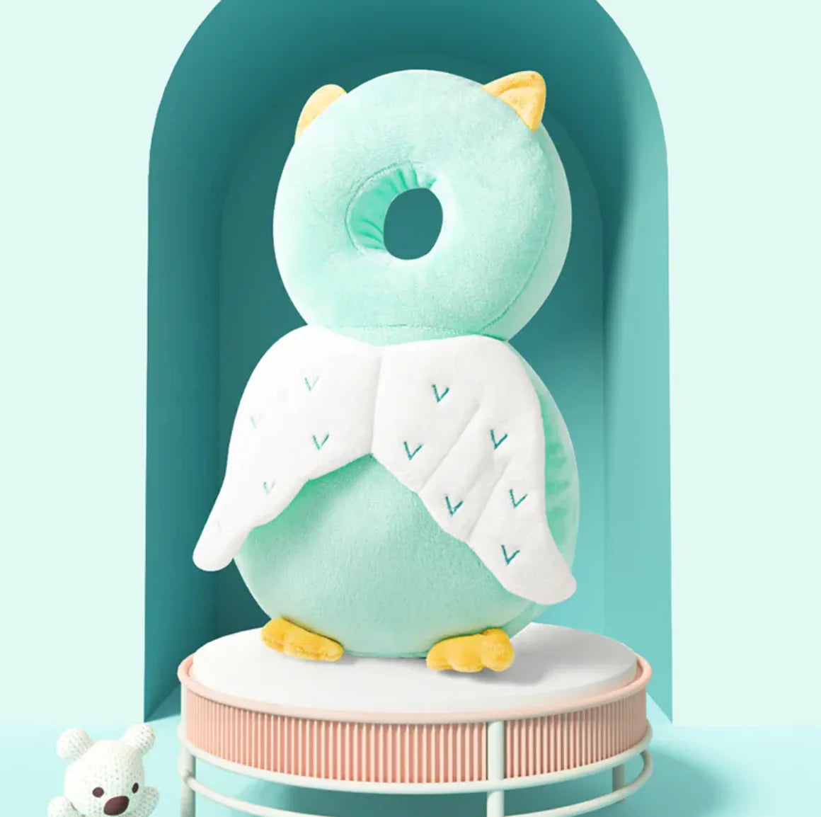 Plush owl toy with a green head and body on a stand against a light blue background