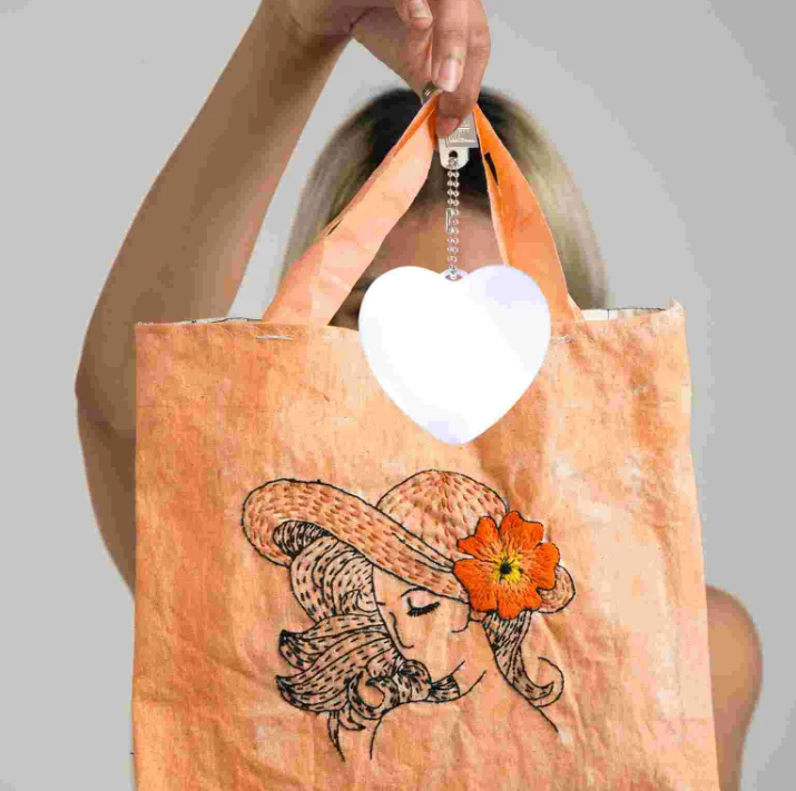 Person holding a tote bag with a design of a woman wearing a hat and flower, against a plain background.