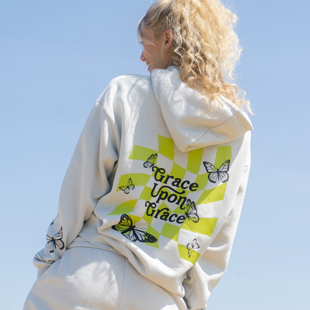 Person wearing a white hoodie with 'Grace Upon Grace' design, standing outdoors with a clear blue sky.